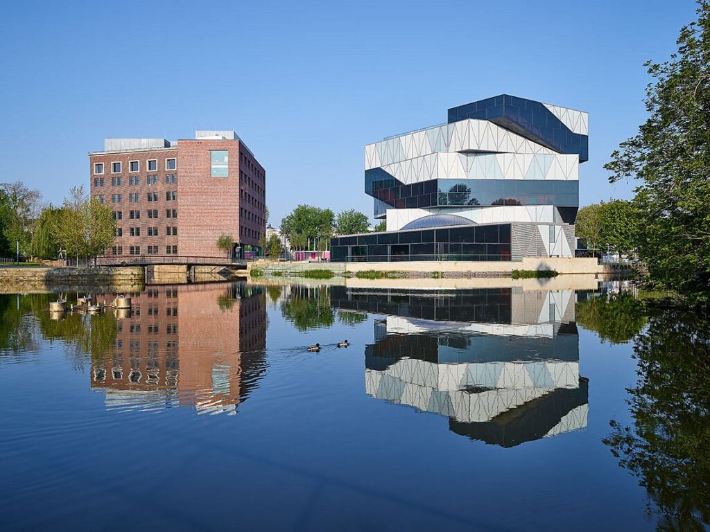 Zwei Gebäude vor einem See. Sie sind das Science Center experimenta in Heilbronn.